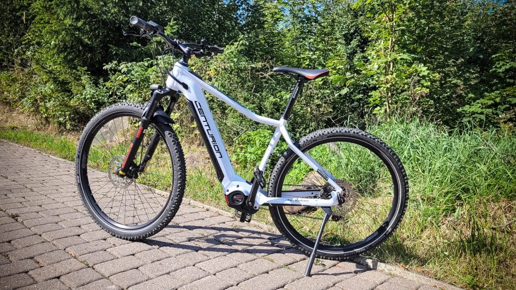 Weißes Fahrrad auf gepflastertem Weg im Grünen.