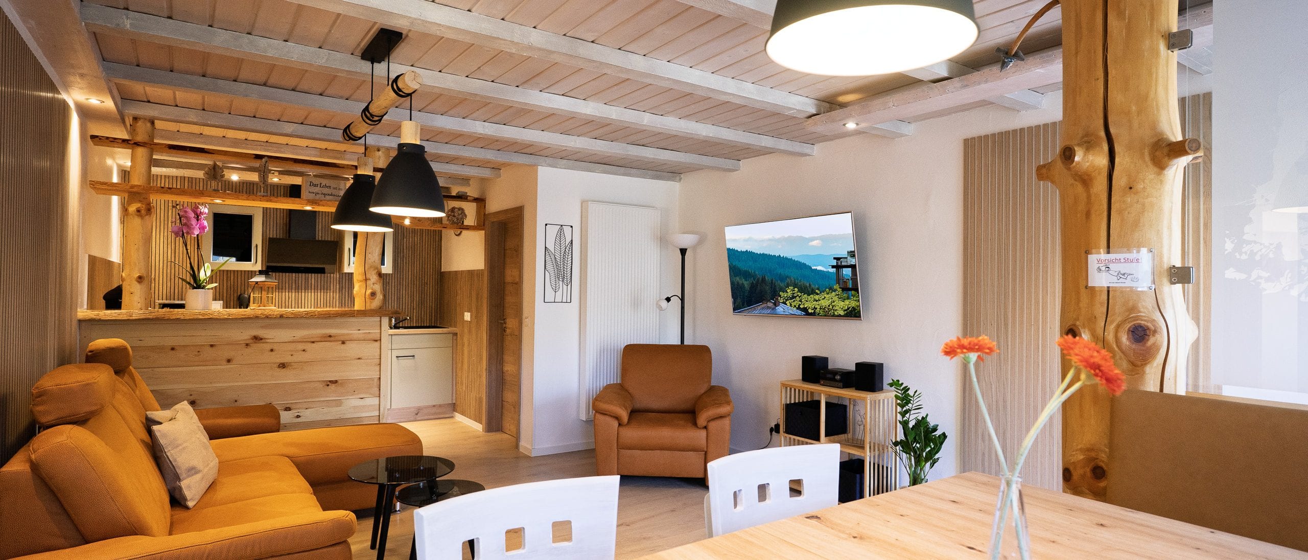 Gemütliches Wohnzimmer mit Holzdecke und offener Küche