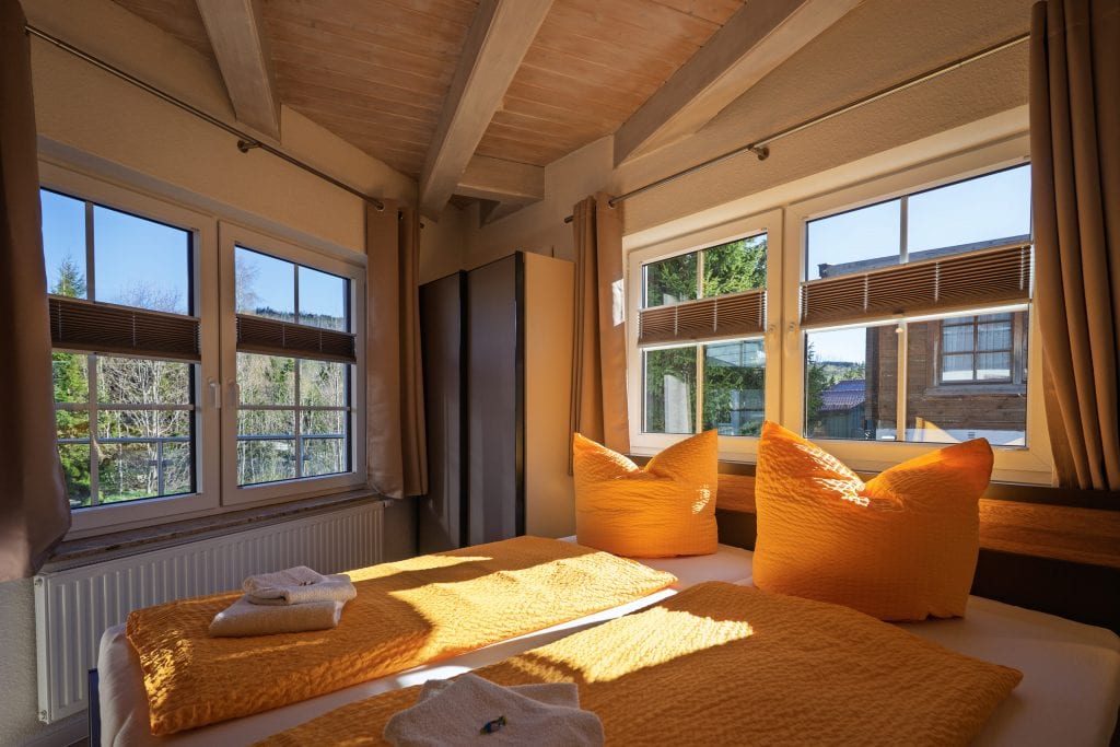 Gemütliches Schlafzimmer mit großen Fenstern und orangefarbener Bettwäsche