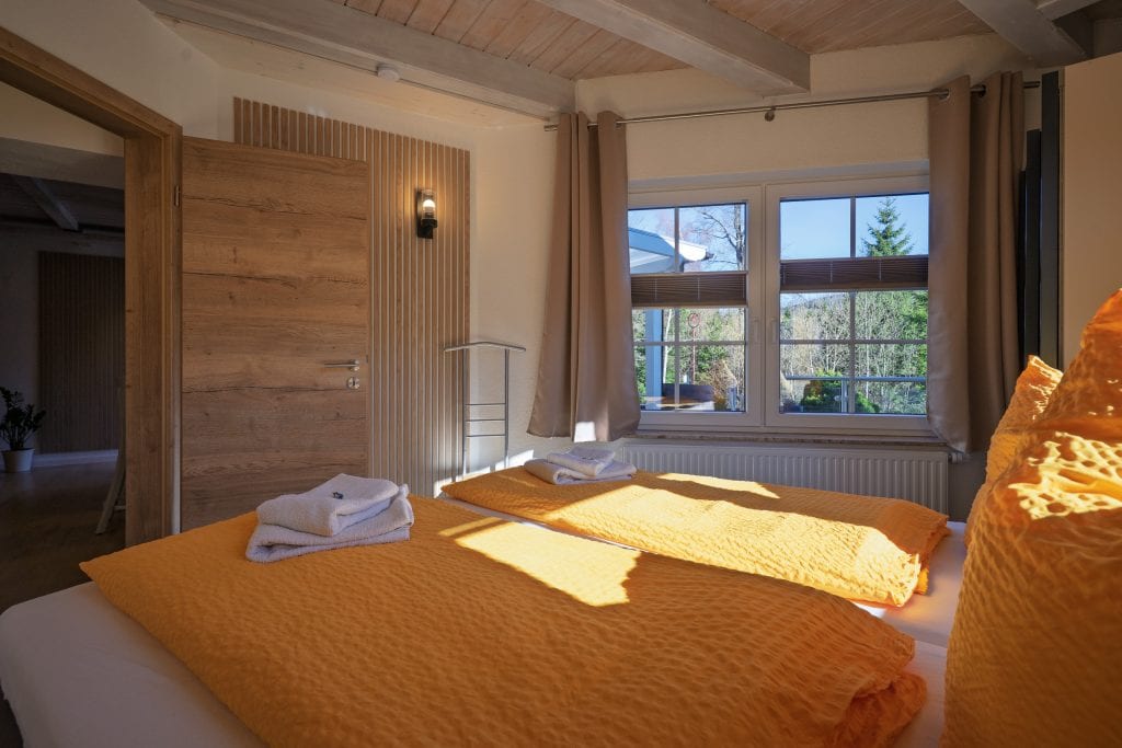 Gemütliches Schlafzimmer mit orangefarbener Tagesdecke und Fensterblick