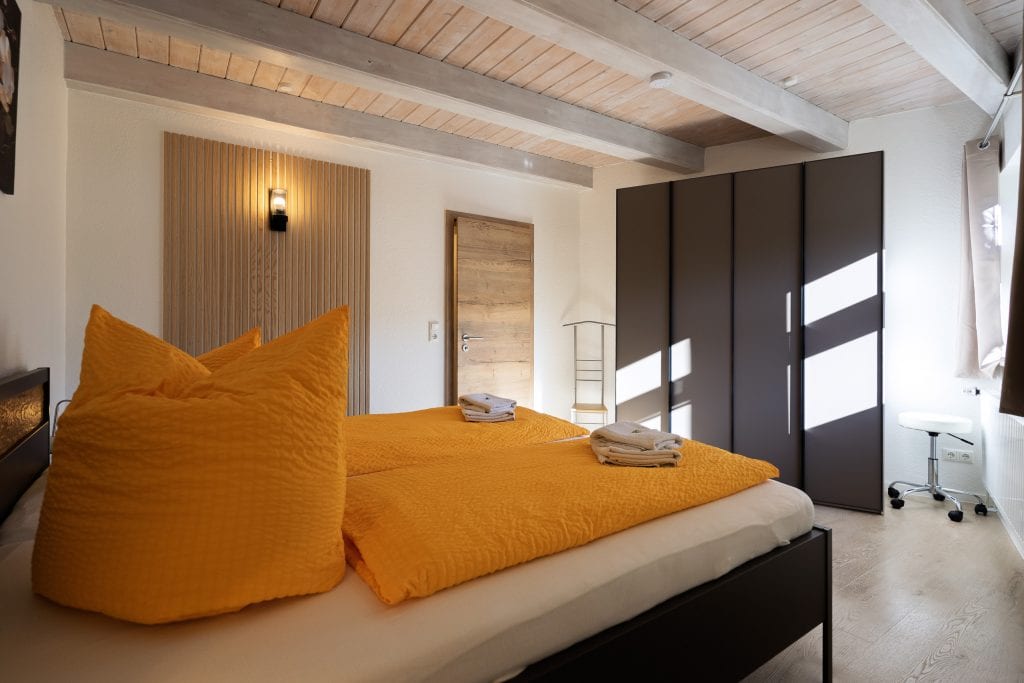 Modernes Schlafzimmer mit orangener Bettwäsche und Holzdecke