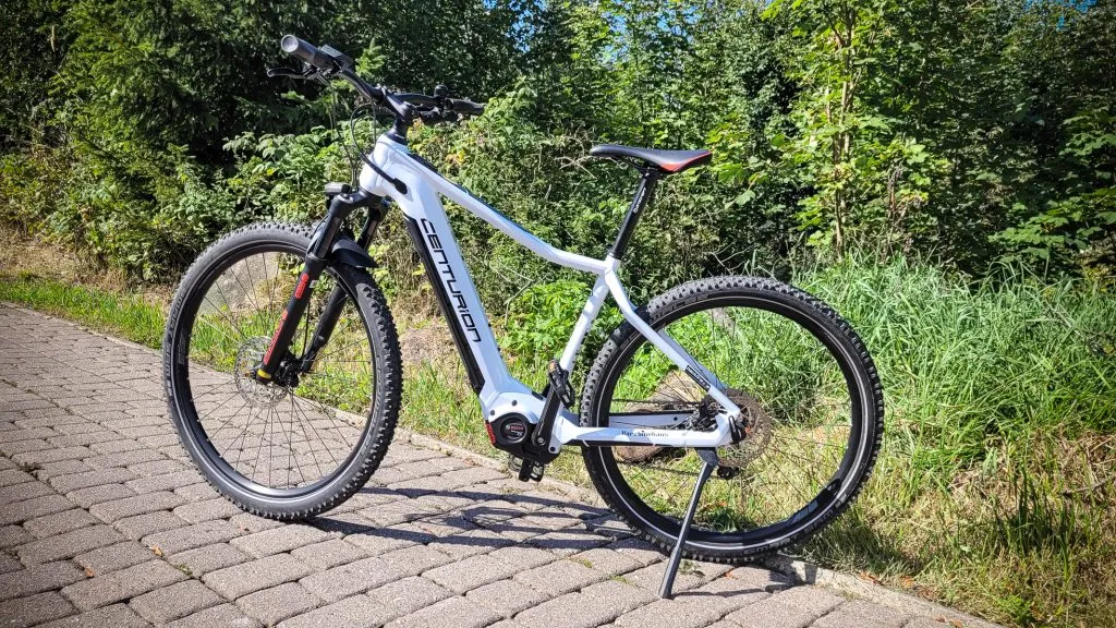 Weißes Fahrrad auf gepflastertem Weg im Grünen.
