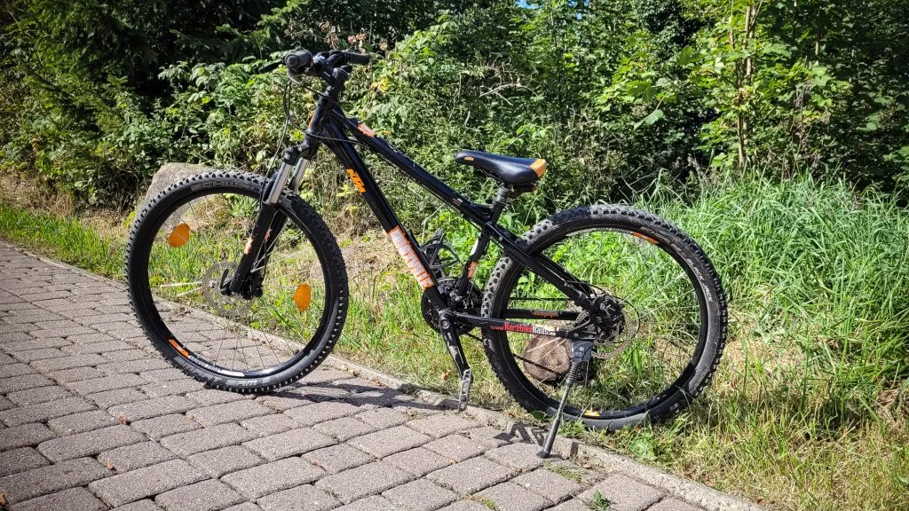 Schwarzes Mountainbike auf parkendem Gehweg.