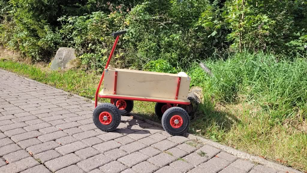 Roter Bollerwagen auf gepflastertem Weg am Waldrand