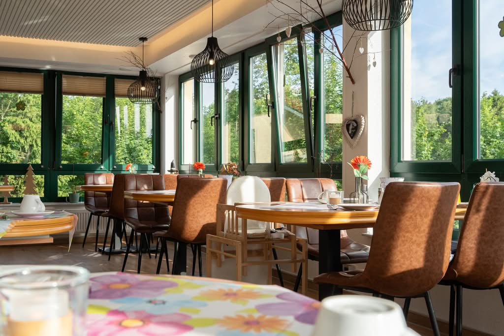 Gemütlicher Frühstücksraum mit großen Fenstern und Lederstühlen