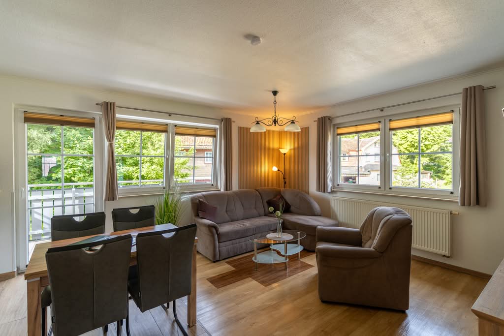 Helles Wohnzimmer mit Sofa, Sessel und großen Fenstern