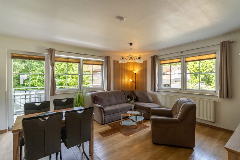 Helles Wohnzimmer mit Sofa, Sessel und großen Fenstern