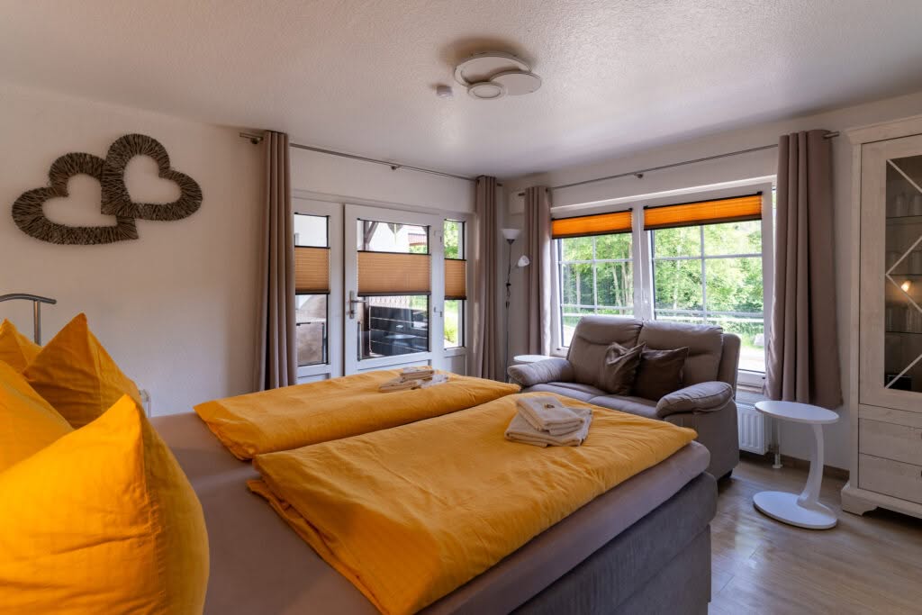 Helles Schlafzimmer mit gelber Bettwäsche und großen Fenstern