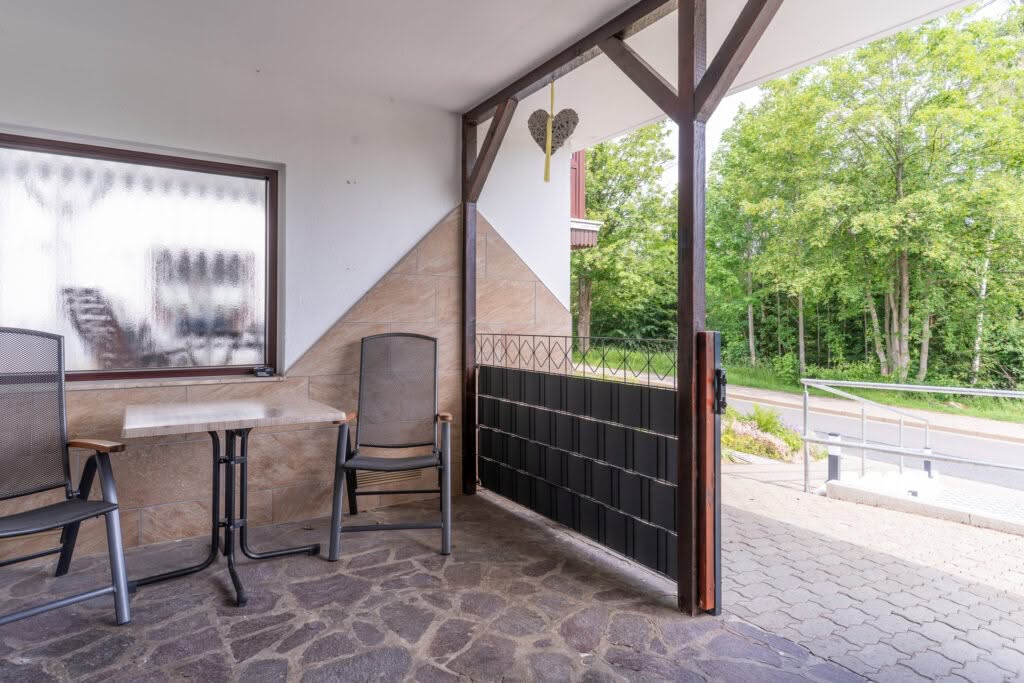 Überdachte Terrasse mit Tisch und zwei Stühlen