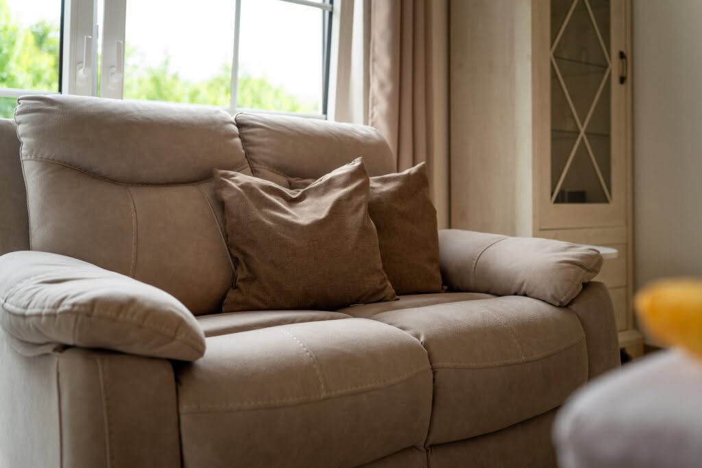 Beiges Ledersofa mit braunen Kissen am Fenster